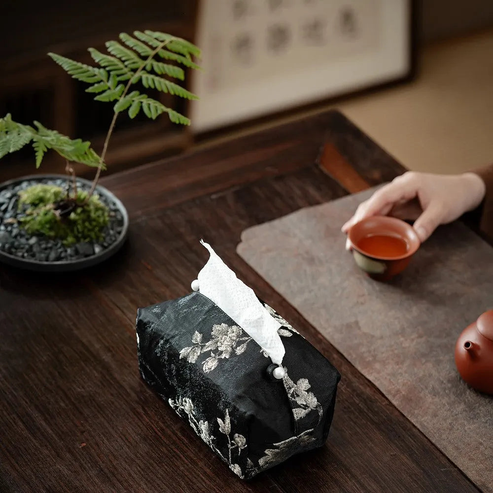 White embroidered plum blossom tissue box cover with fabric texture, shown next to a standard tissue carton for scale.