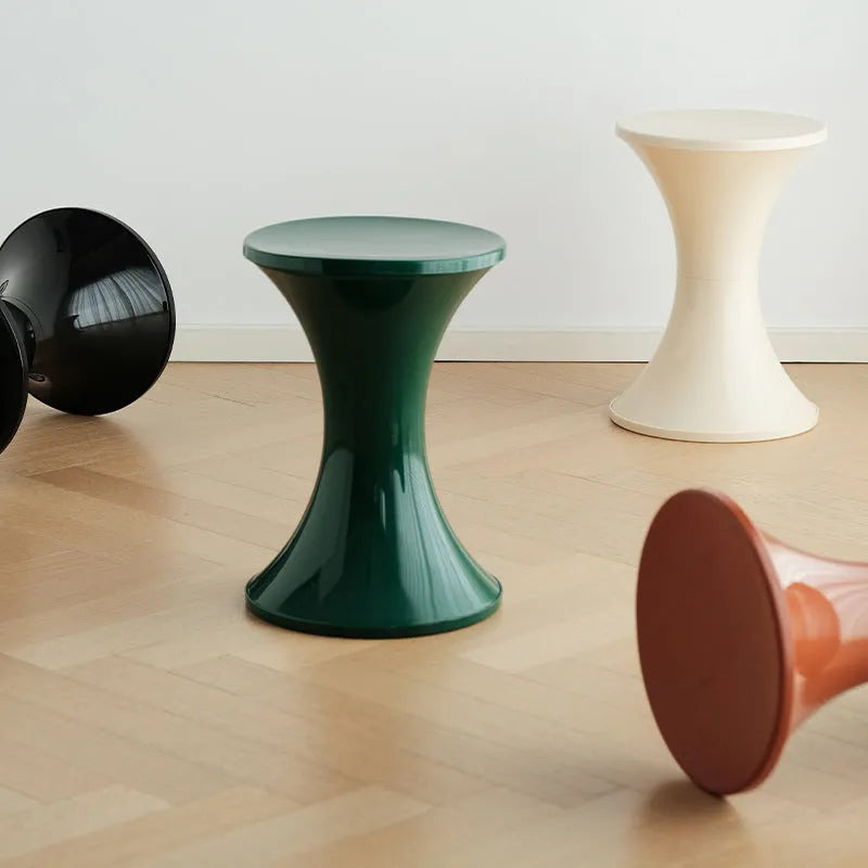 Plastic hourglass-shaped shoe changing stool shown in green, placed on a wooden floor.