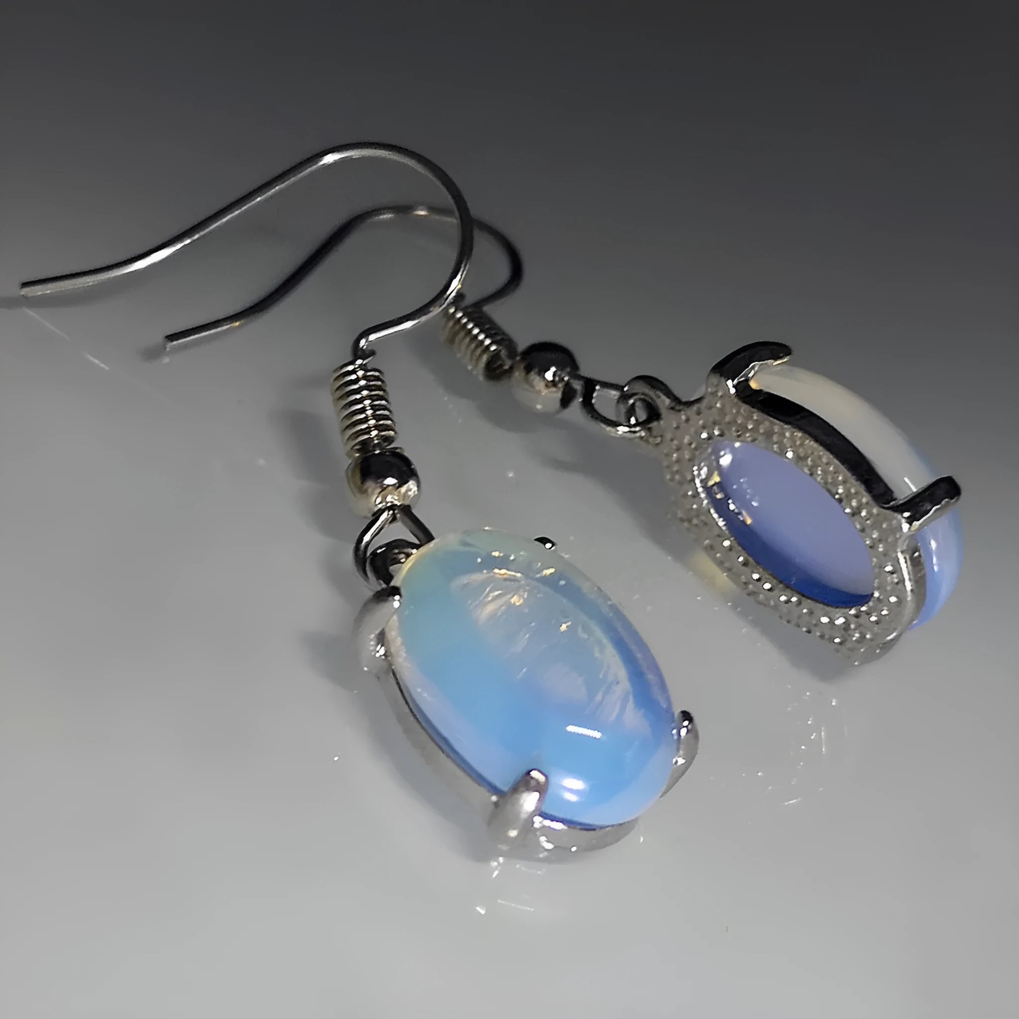 Close-up of moonlight white opal drop earrings with a cross pendant on an alloy post.