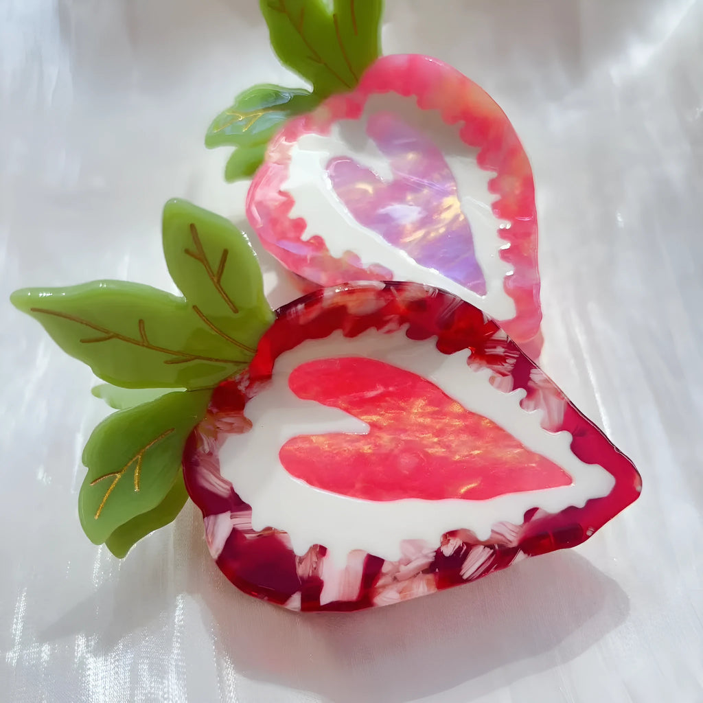 Close-up of a handmade strawberry decorative hair clip on a pink background.