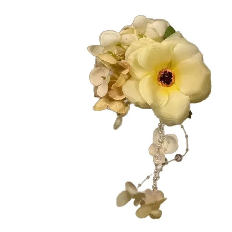 Close-up of a women's hair clip with a white pearl, yellow fabric flowers, and a long yellow tassel on a dark background.