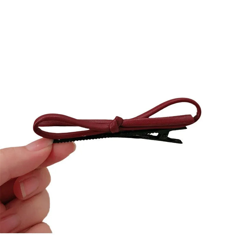 Wine red genuine leather bow attached to a metal hair clip, shown on a background.