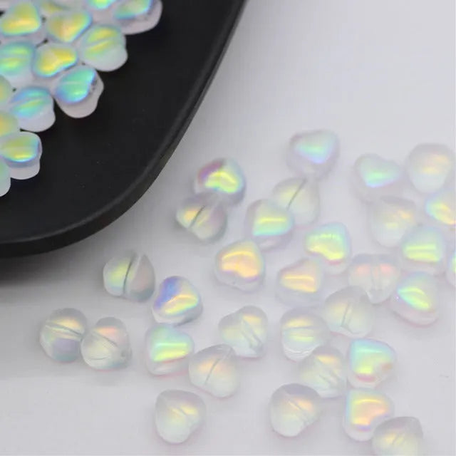 Twenty transparent love heart shaped spacer beads in assorted colours on a white background.