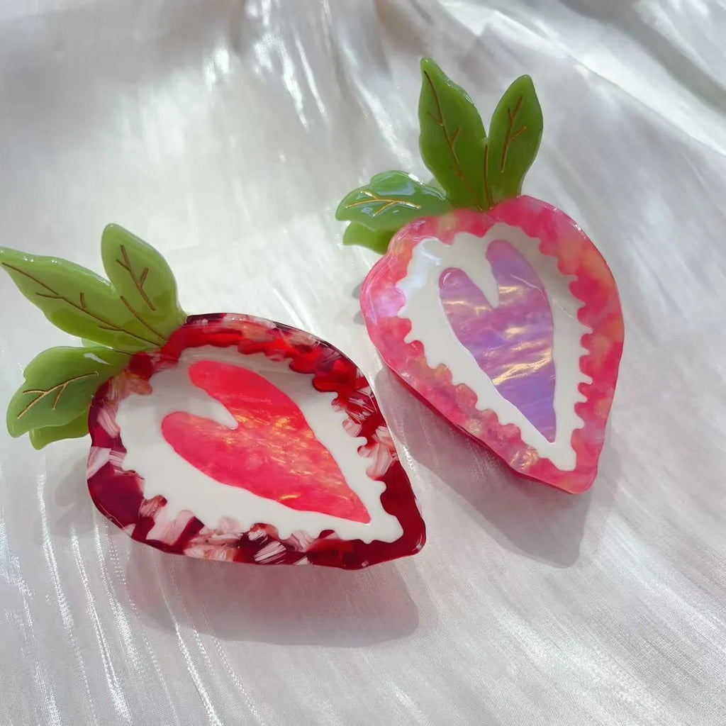Close-up of a handmade strawberry decorative hair clip on a pink background.