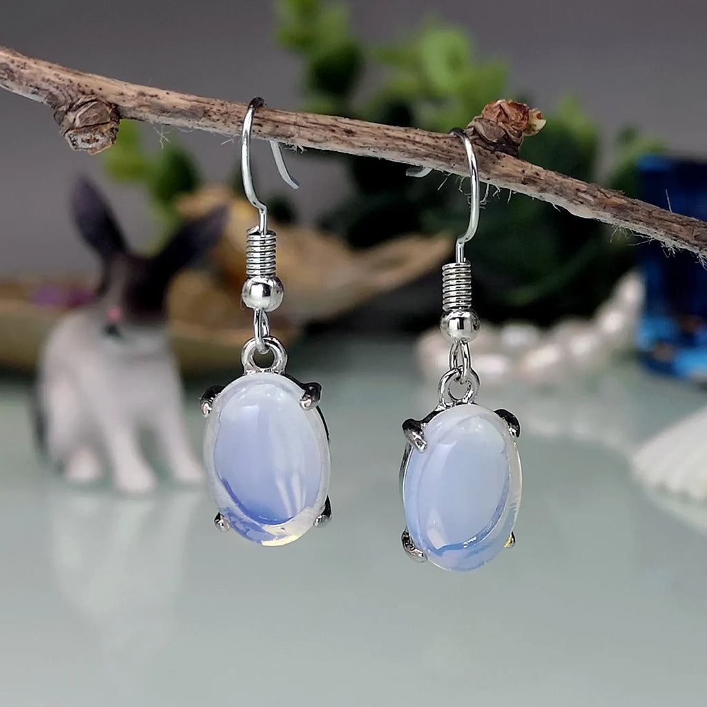 Close-up of moonlight white opal drop earrings with a cross pendant on an alloy post.