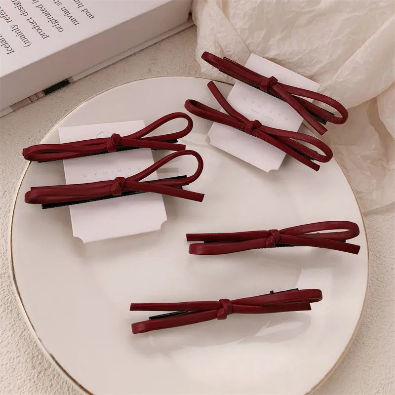 Wine red genuine leather bow attached to a metal hair clip, shown on a background.