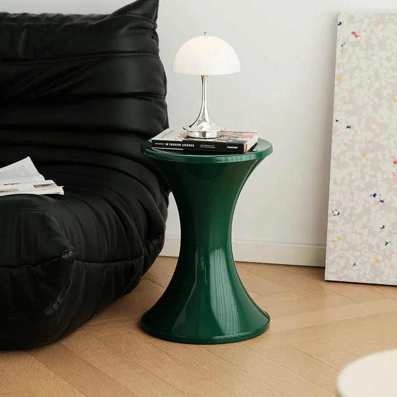 Plastic hourglass-shaped shoe changing stool shown in green, placed on a wooden floor.