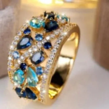 Women's round hollow fashion ring in gold or platinum plating with a central clear or blue crystal stone.