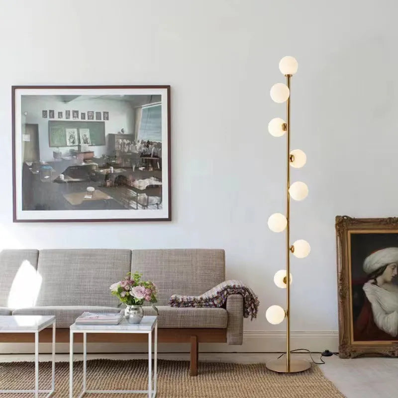 Tall modern floor lamp with slender iron frame, glass shade, and solid circular base in a minimalist living room setting.