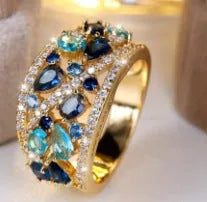 Women's round hollow fashion ring in gold or platinum plating with a central clear or blue crystal stone.