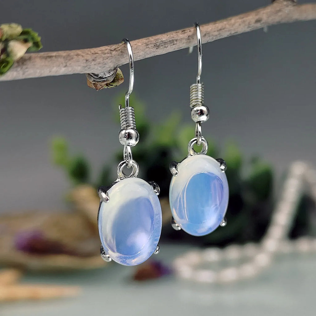 Close-up of moonlight white opal drop earrings with a cross pendant on an alloy post.