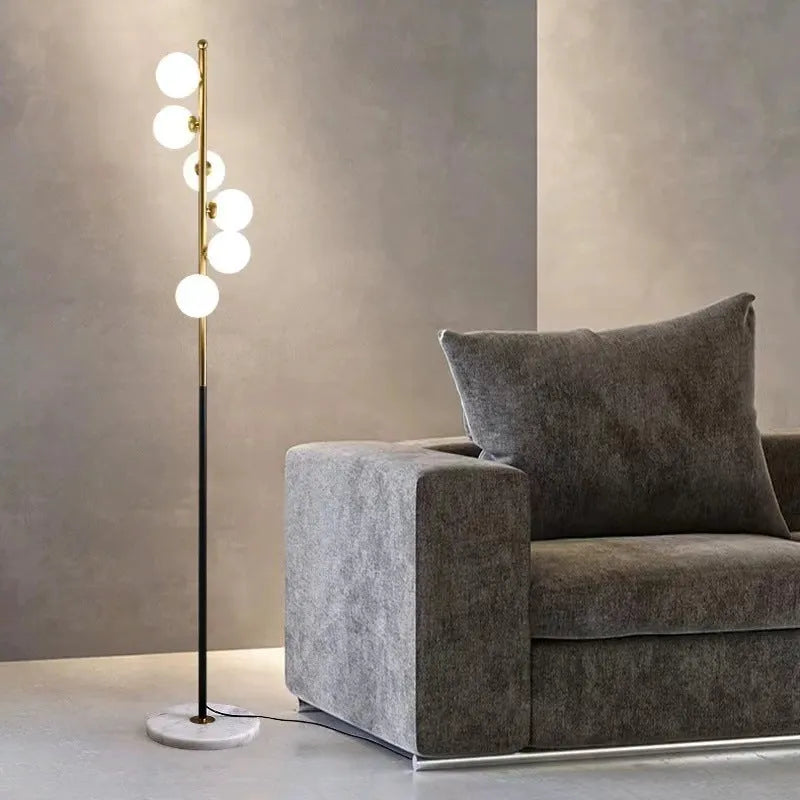 Tall modern floor lamp with slender iron frame, glass shade, and solid circular base in a minimalist living room setting.