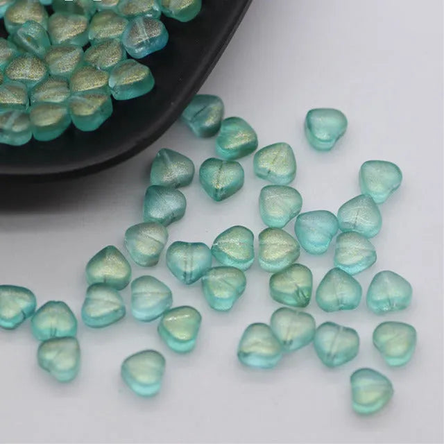 Twenty transparent love heart shaped spacer beads in assorted colours on a white background.