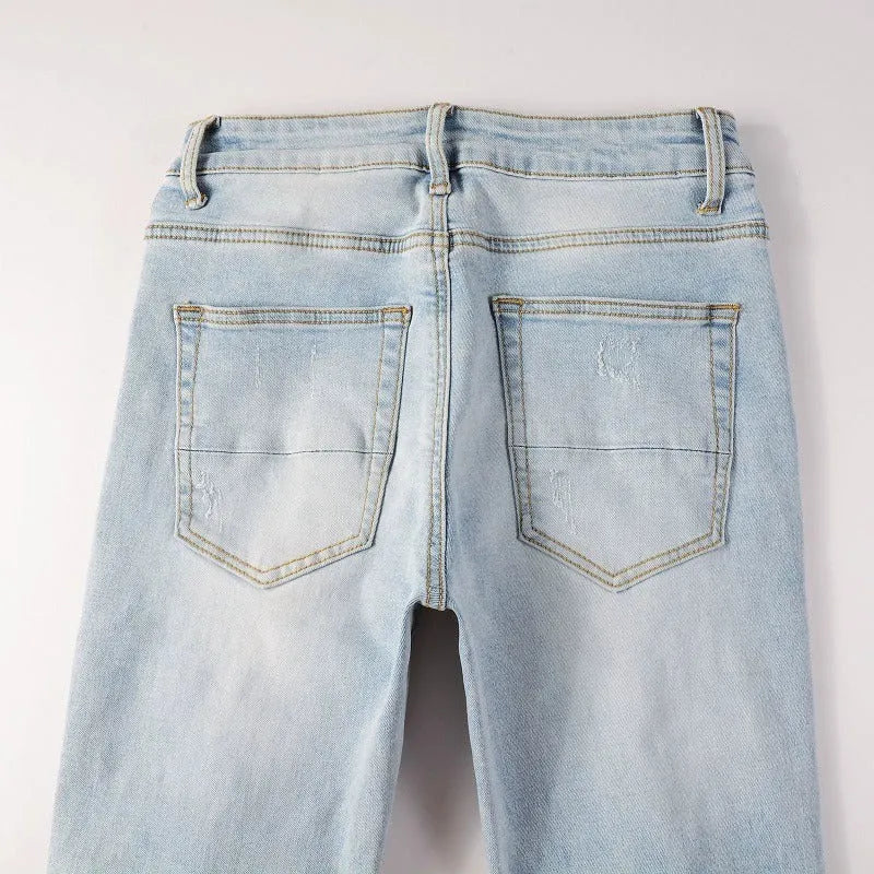 Light blue slim fit men's jeans with patch details, holes, and enzyme-washed finish