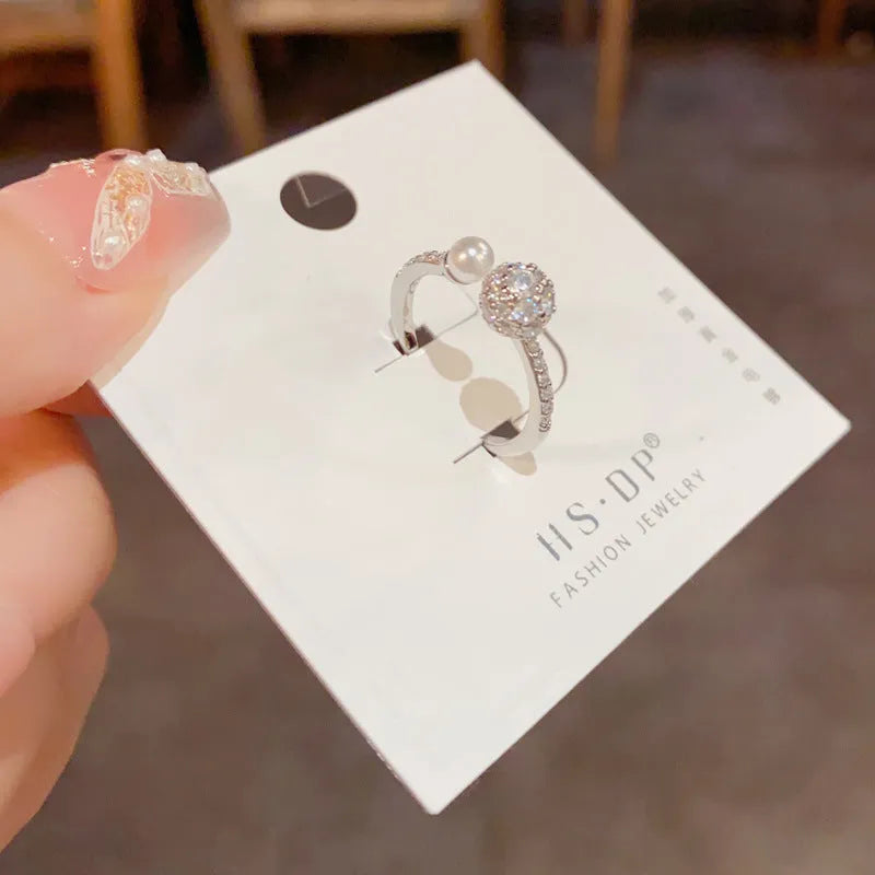 Gold or silver coloured open-end women's ring with round zircon stones and pearl detailing on a geometric band.