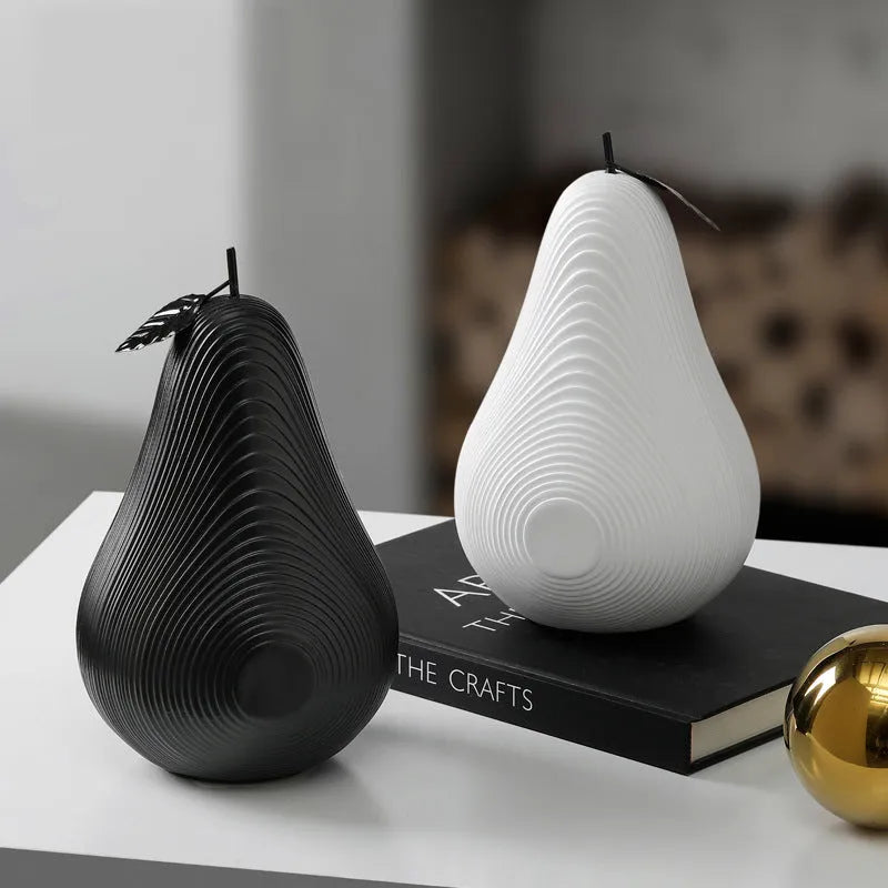 A black resin apple figurine and a white resin pear figurine on a wooden surface.