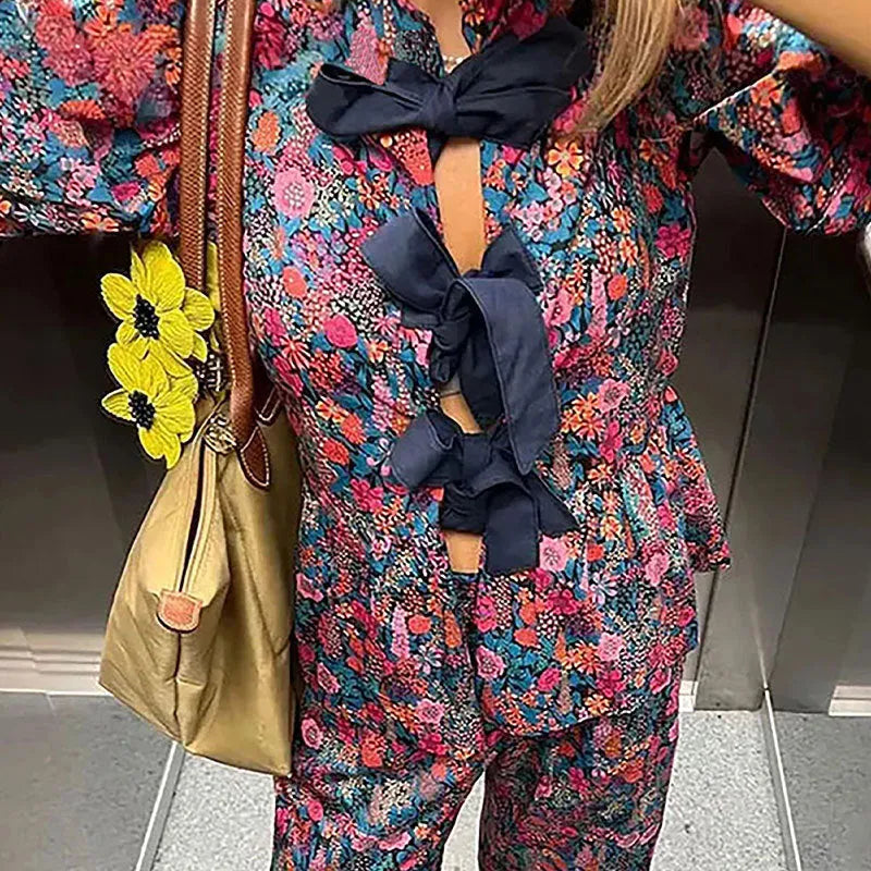 Women's floral printed trousers suit with a tie-neck blouse featuring puff sleeves and matching trousers.