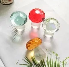 Handcrafted white crystal mushroom decoration in four colours on a wooden surface.