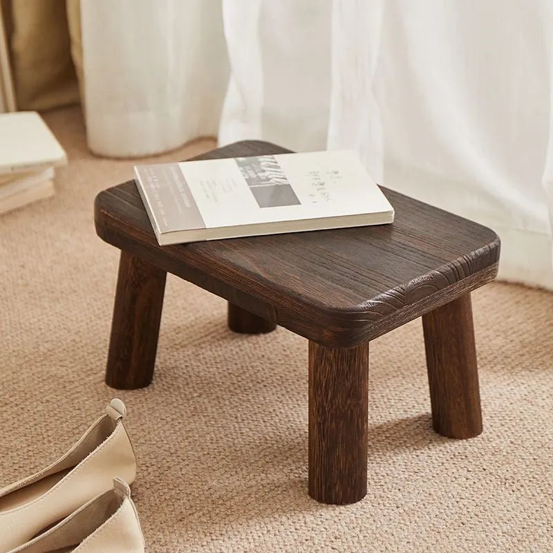 Solid wood shoe changing stool with a distressed finish and angular bracket frame.