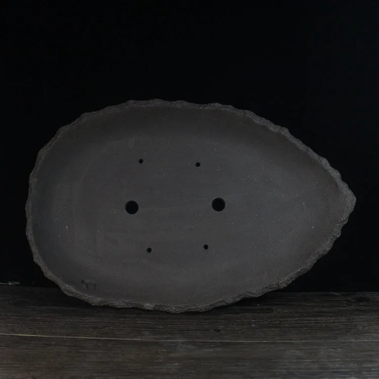 Handmade purple clay flower pot with drainage hole on a wooden floor