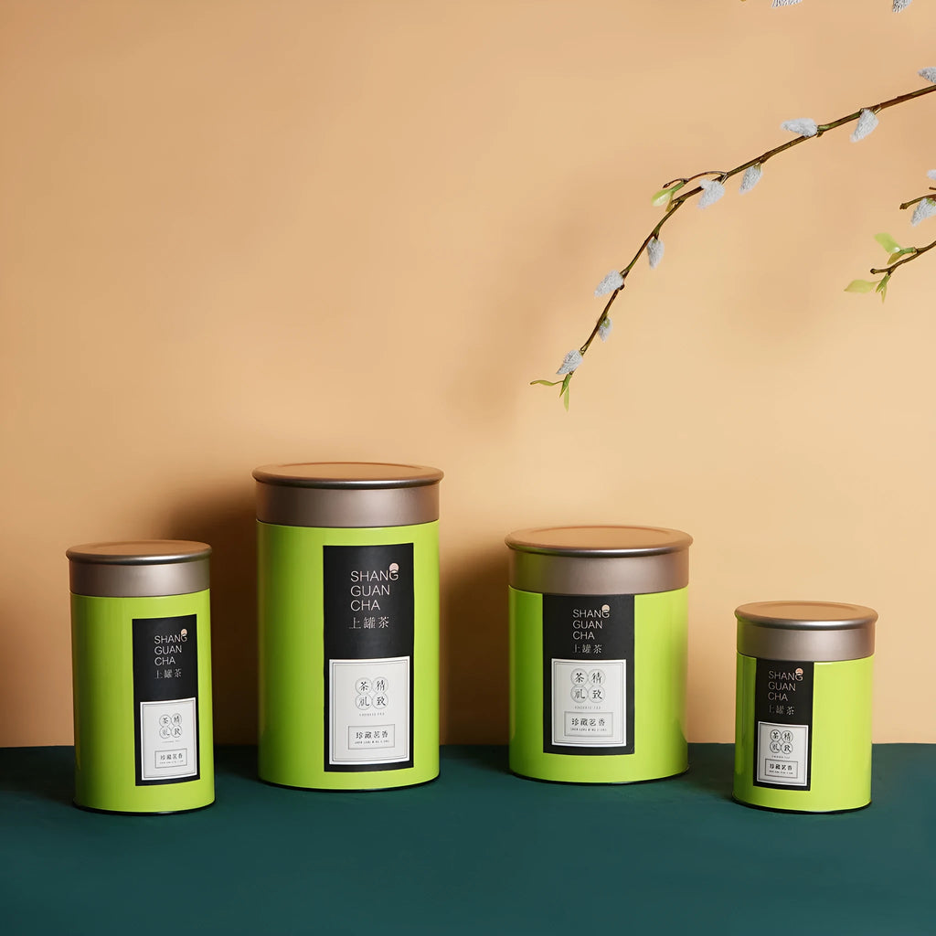 Green tinplate sealed tea storage box with black lid on a wooden surface.