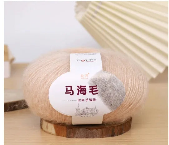 A ball of mohair yarn in a selected colour next to a hand-woven scarf example, showcasing the DIY kit.