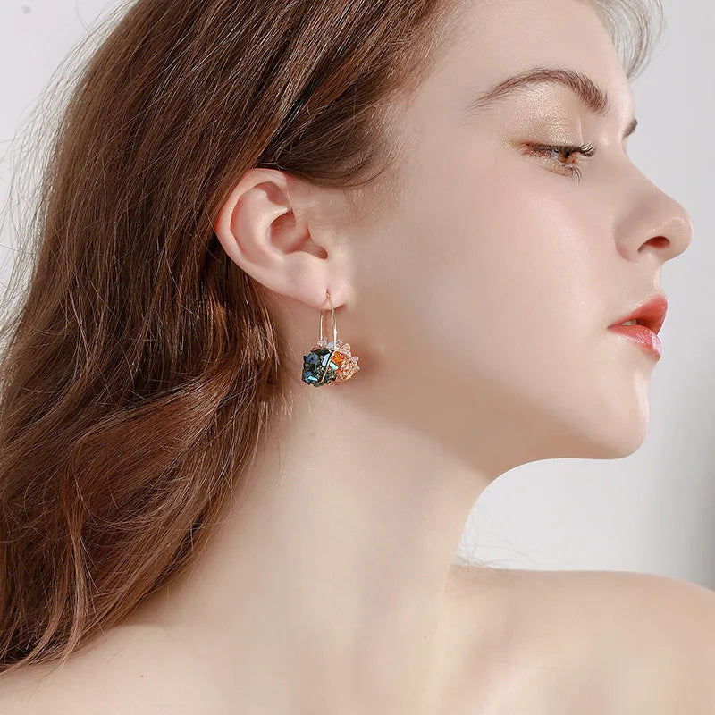 Pair of champagne gold geometric quadrilateral drop earrings on a neutral background