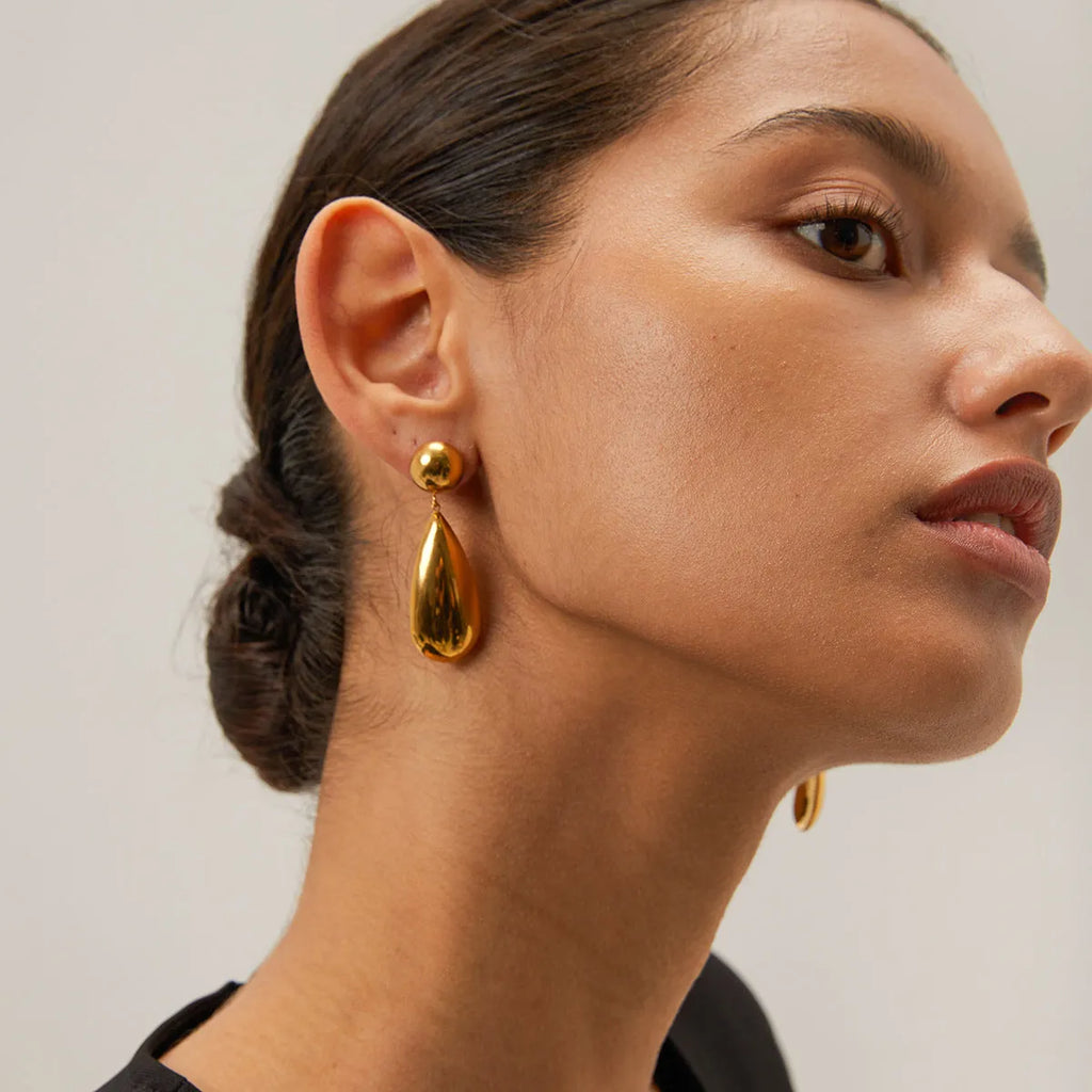 A pair of gold-coloured stainless steel pendant earrings with a geometric water drop hemisphere shape.