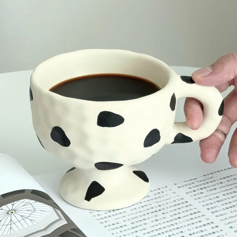 A hand-pinched ceramic mug with an irregular shape in a solid colour, shown on a table.