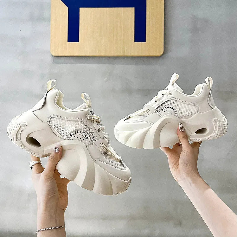 Women's pink sneakers with a cross strap and thick sole on a neutral background.