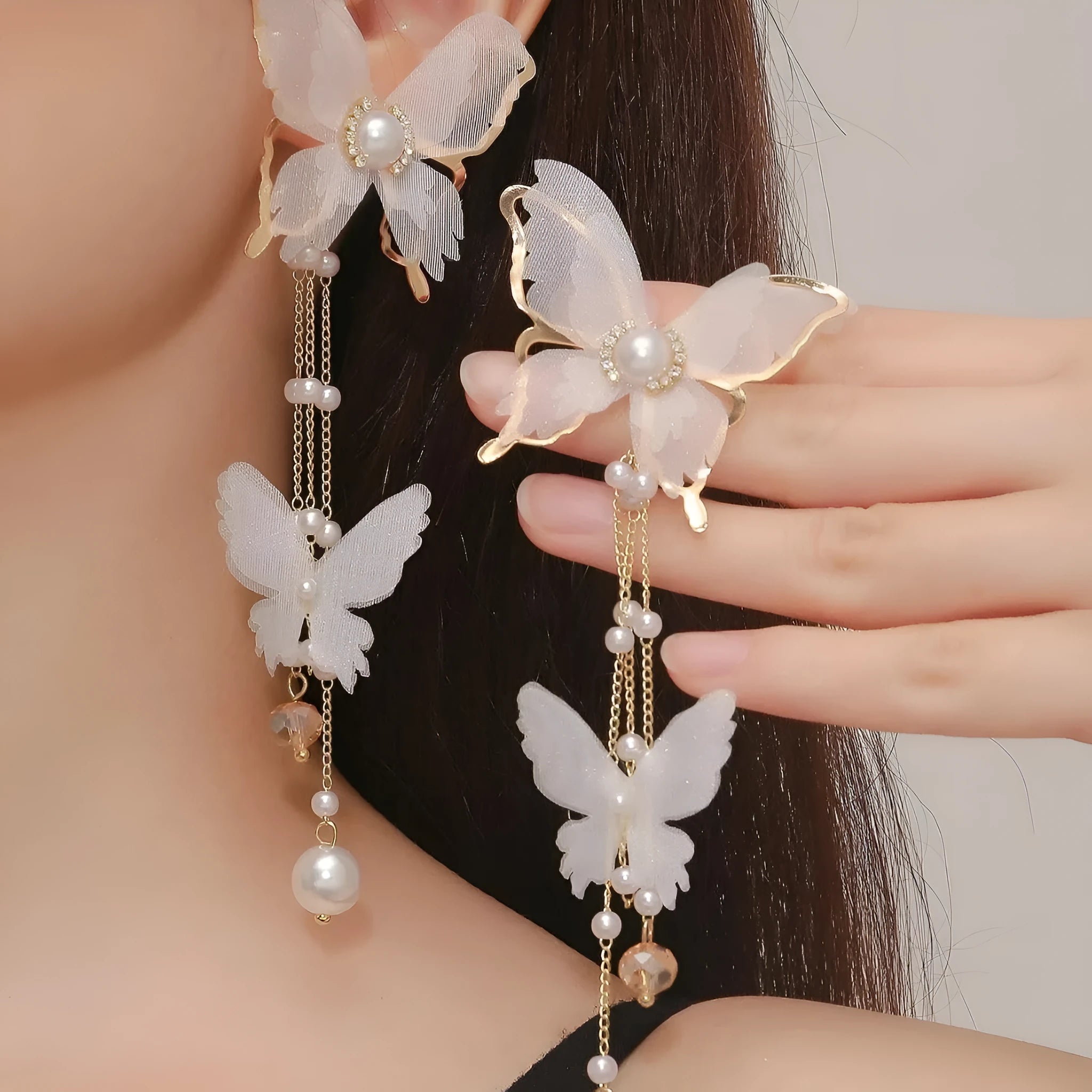 White butterfly-shaped drop earrings with rhinestones, a long chain tassel, and a pearl tip on a white background.