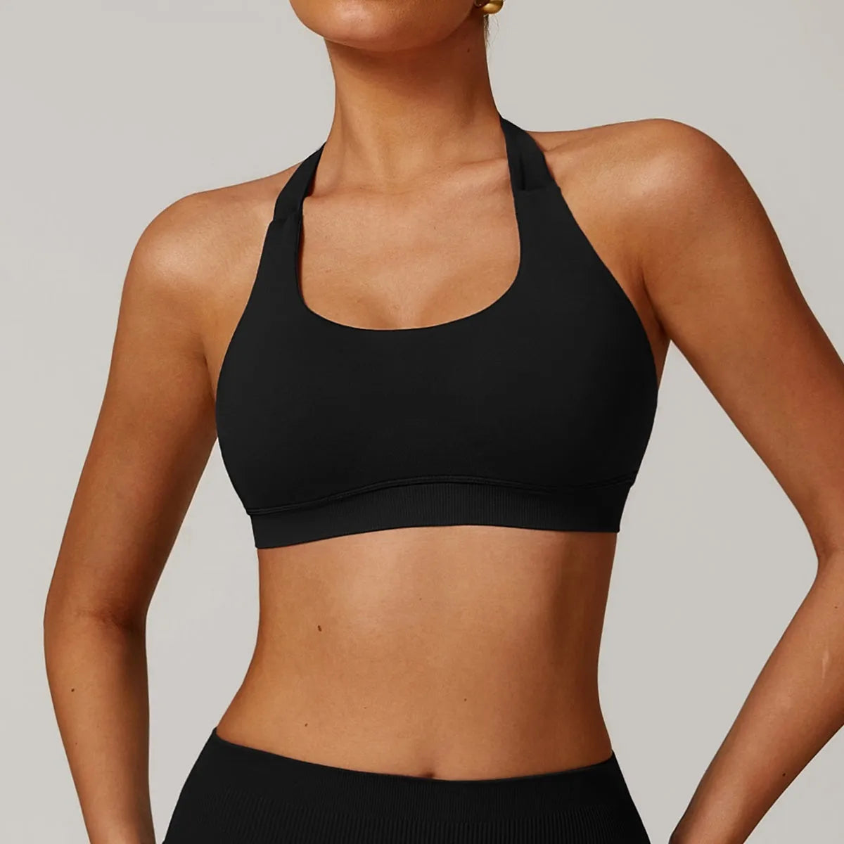 Women's black halter-neck sports bra with removable padding on a grey background.