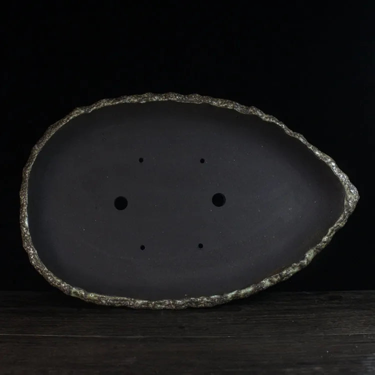 Handmade purple clay flower pot with drainage hole on a wooden floor