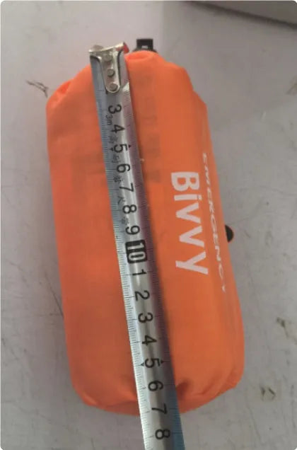 Orange and green emergency tent, sleeping bag, and raincoat kit for outdoor survival.