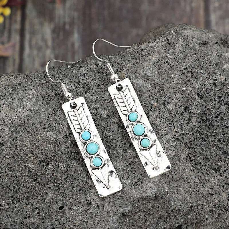 Silver geometric drop earrings with turquoise inlaid accents on a plain background