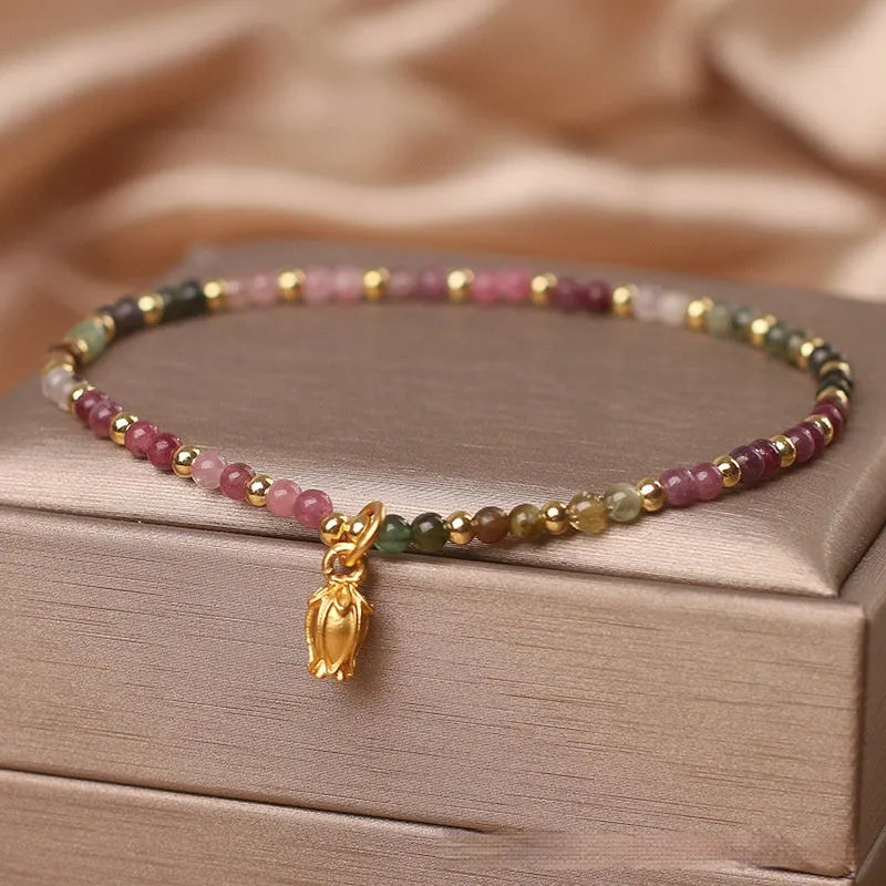 Close-up of a women's beaded anklet with polished tourmaline stones and a detailed metal floral clasp.