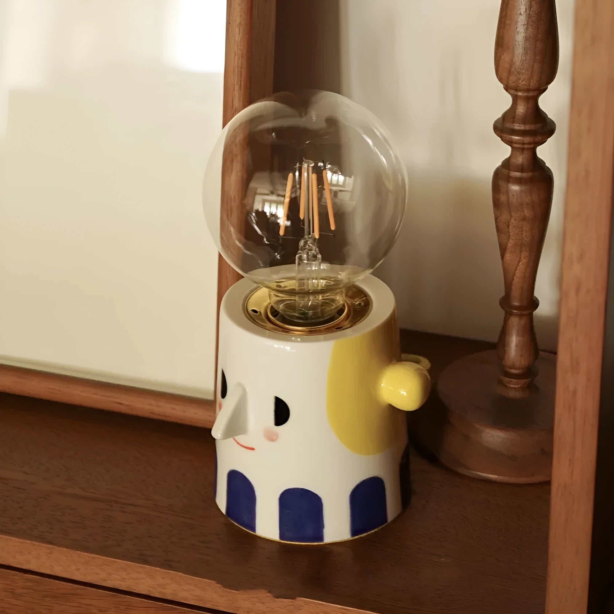 Handmade ceramic bedside lamp with a white ball headlight on a wooden table.