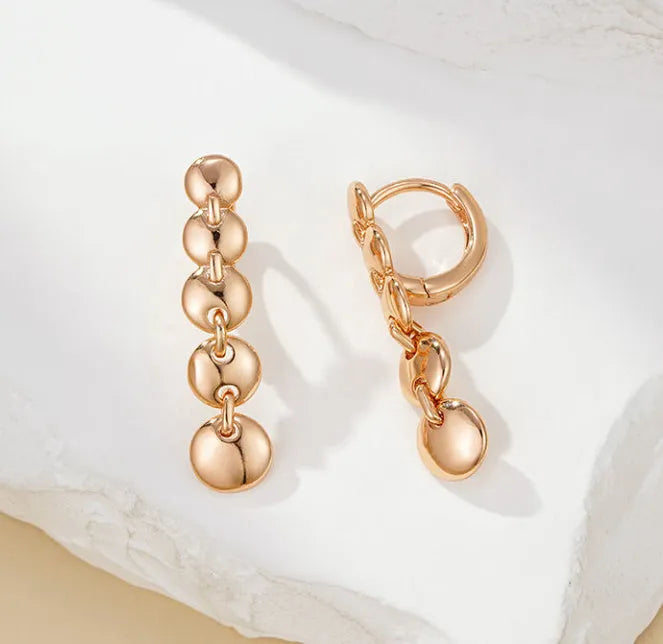 A pair of long, round, woven copper earrings with a gold finish, showing textured detail.