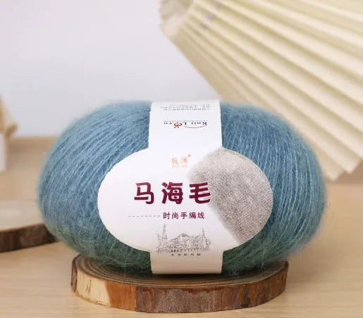 A ball of mohair yarn in a selected colour next to a hand-woven scarf example, showcasing the DIY kit.