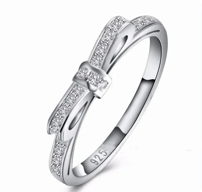 Close-up of a silver bow-shaped ring with sparkling clear zircon crystals on a person's finger.