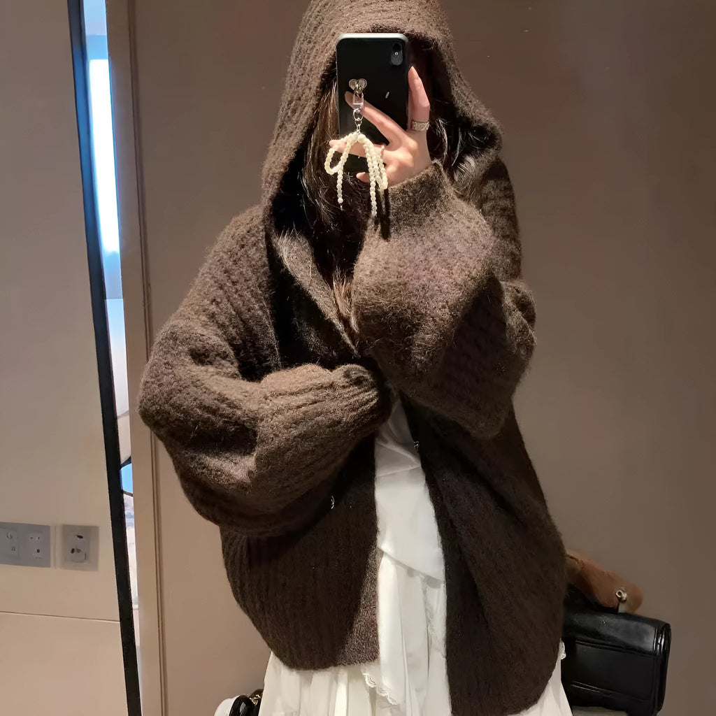 A woman wearing a thick, dark grey hooded cardigan with a loose, longline fit.