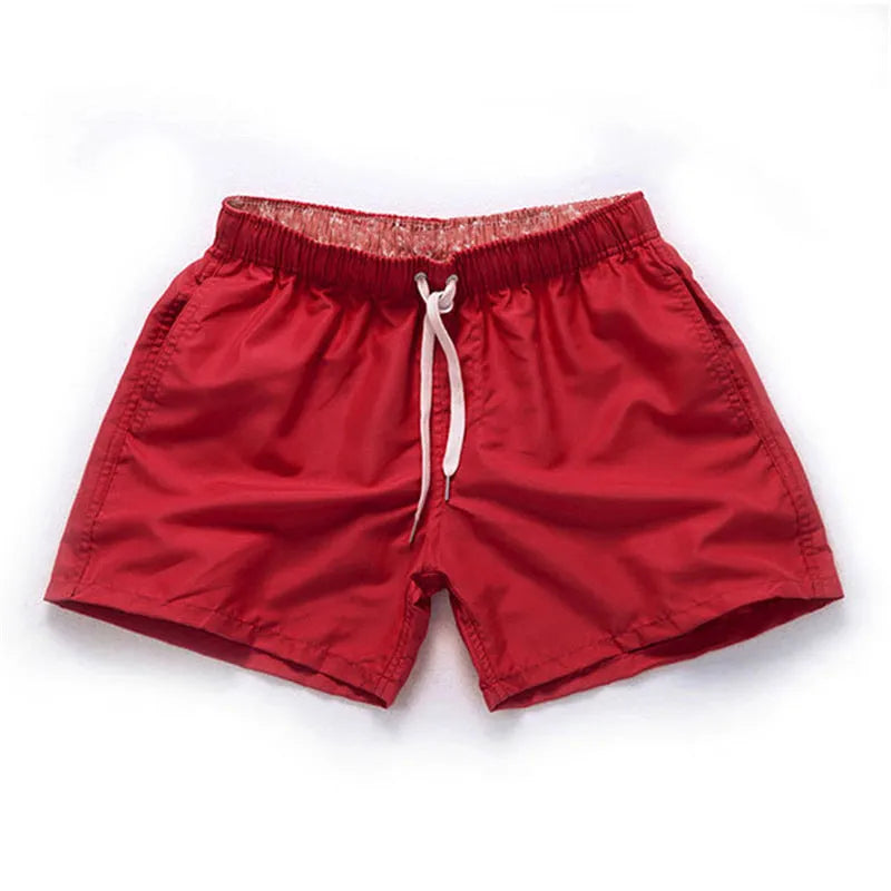 Men's polyester surf shorts in multiple colours on a beach background, showing straight leg design.