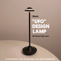 Modern UFO-shaped metal table lamp in black on a wooden desk, showcasing its rechargeable, touch-dimming design.
