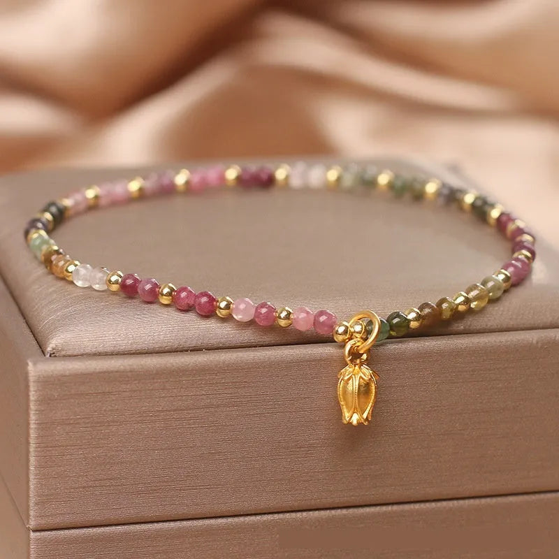 Close-up of a women's beaded anklet with polished tourmaline stones and a detailed metal floral clasp.