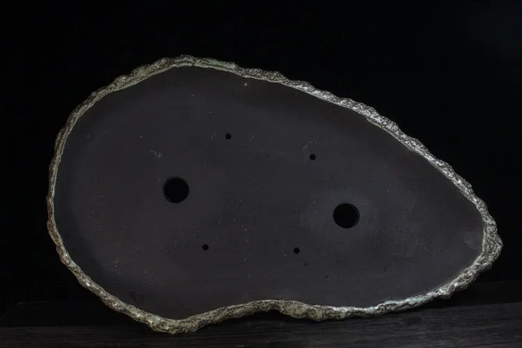 Handmade purple clay flower pot with drainage hole on a wooden floor