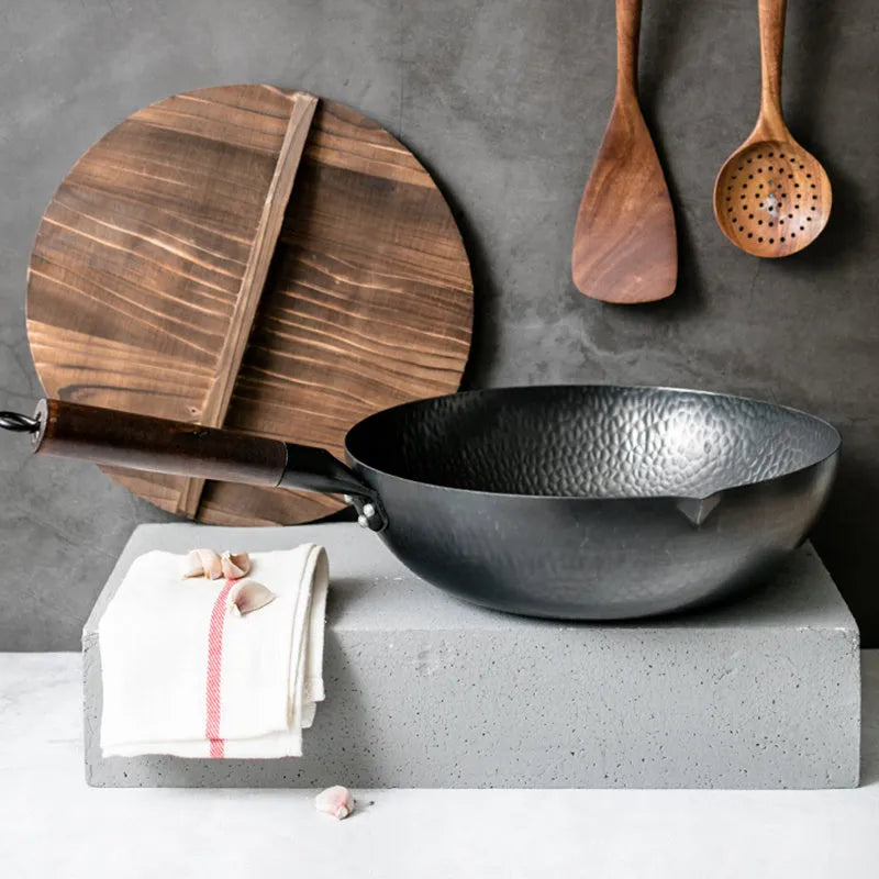 Handmade traditional black cast iron wok with wooden handle on a kitchen counter.