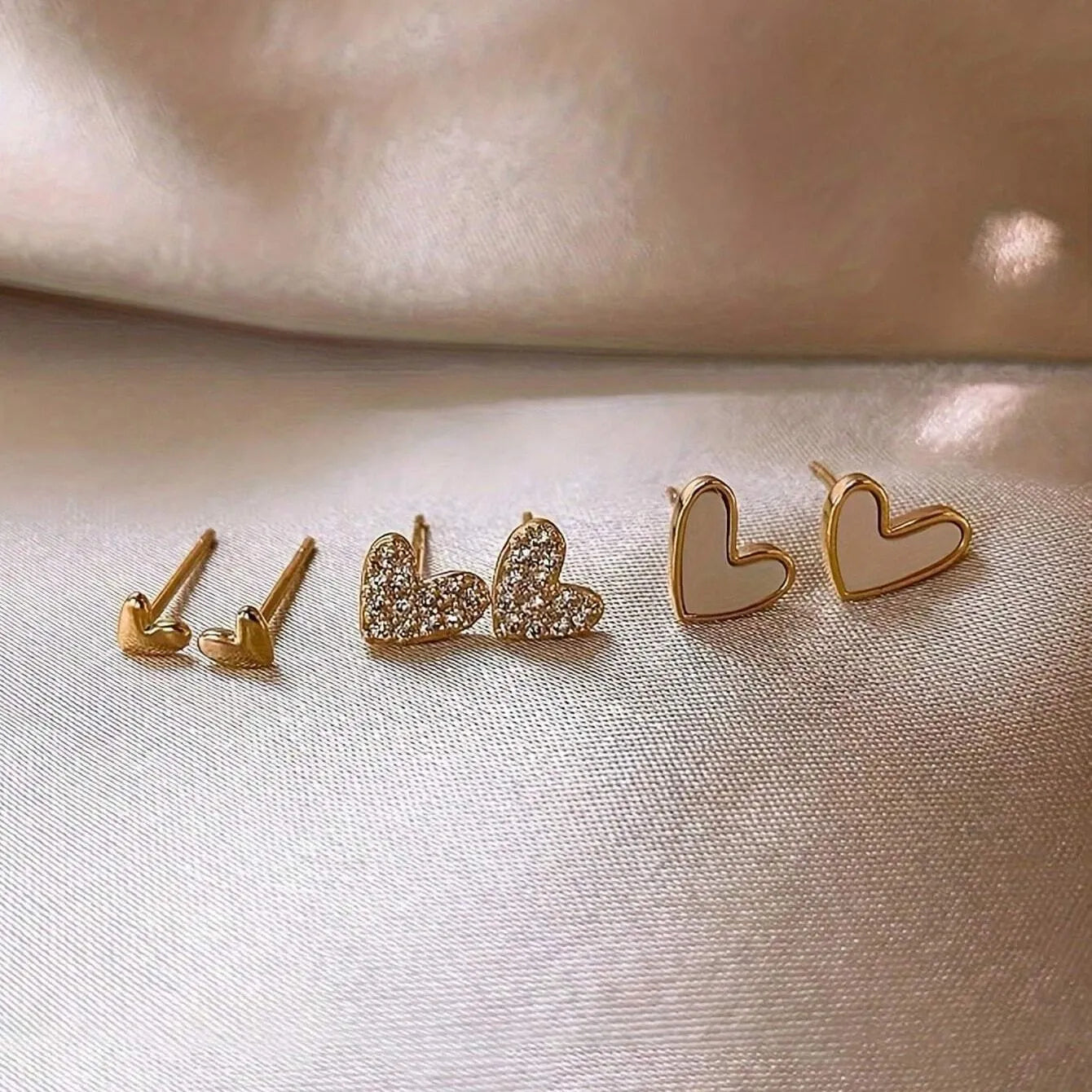 Three pairs of heart-shaped alloy earrings in gold, black, black and white, and pink colours