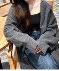 A woman wearing a long, loose, hooded knitted cardigan in a solid colour, demonstrating its below-the-knee length.