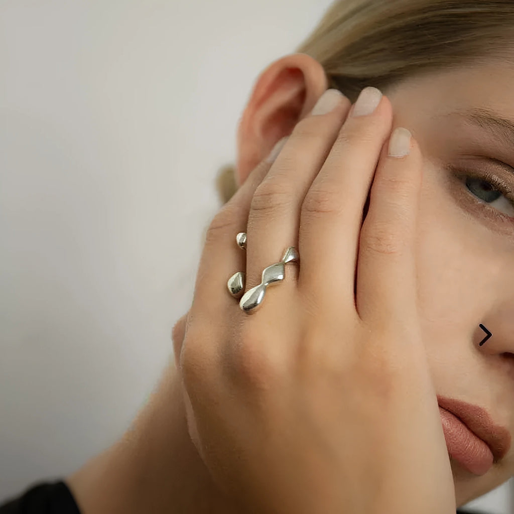 Gold tone brass ring with open circle design and central sphere on a person's finger.