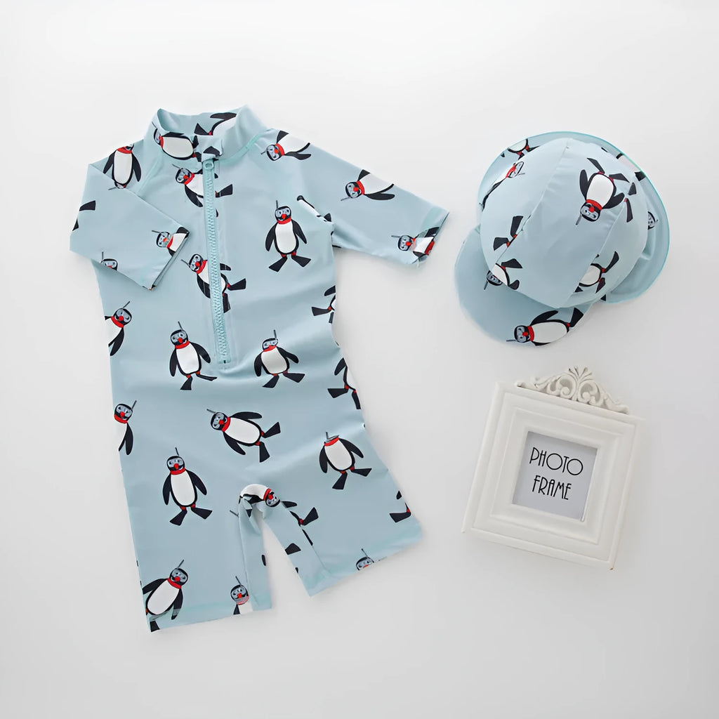 Toddler boy wearing a penguin print long sleeve one-piece swimsuit and matching swimming cap.